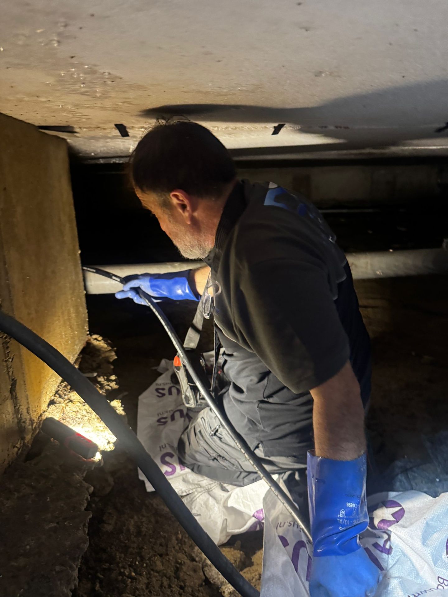 Specialist Lekdetectie De Dijk inspecteert leiding in kruipruimte met zaklamp